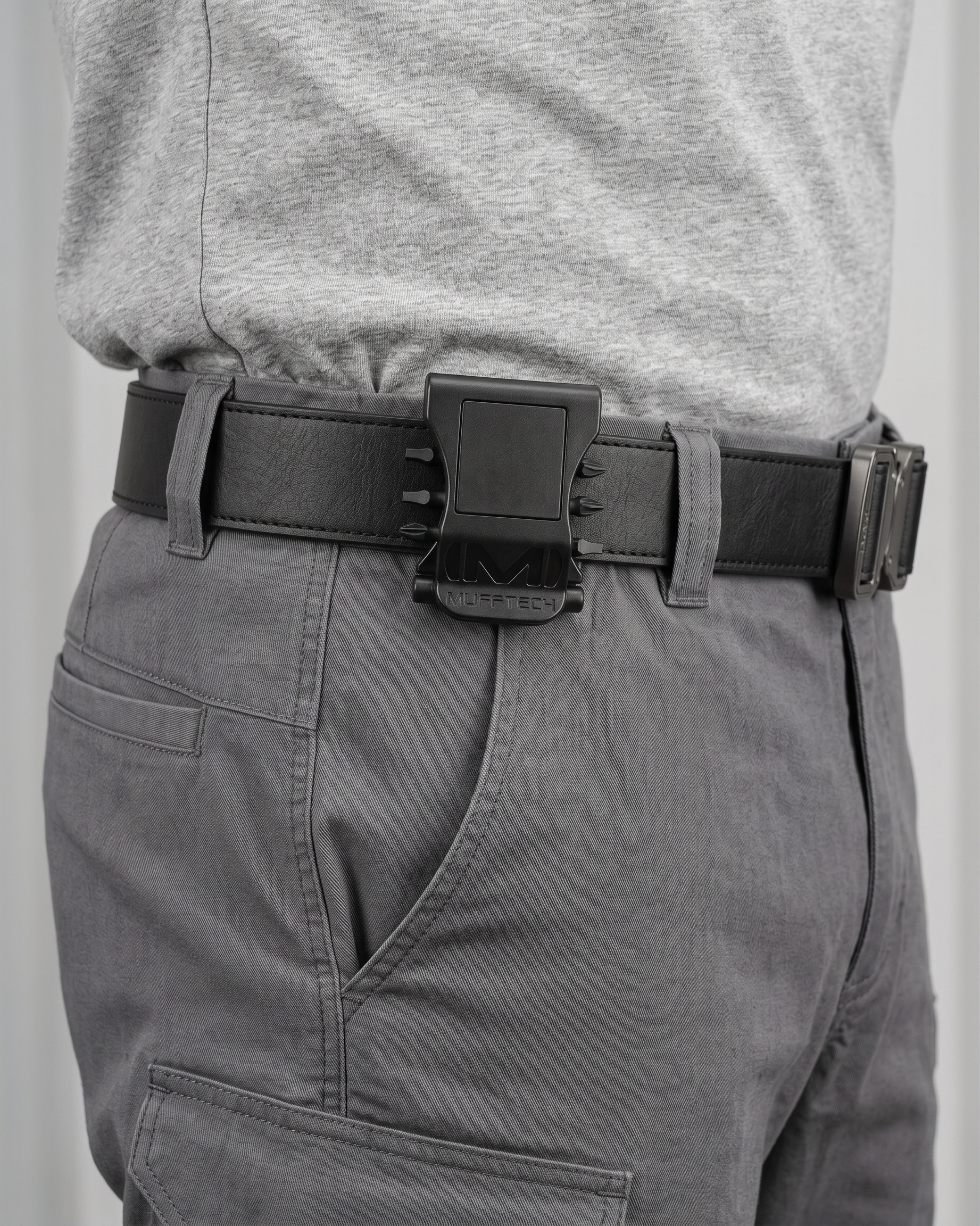 Person wearing a black belt with a large buckle on gray pants against a plain background